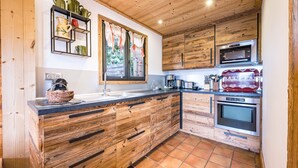 A kitchen with wooden cabinetry, a black countertop, a microwave, an oven, and a window with curtains. - Chalet Farapreu – Alpine Escape and Absolute Comfort in Manigod (Manigod)