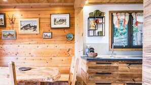 A wooden interior with a dining table, chairs, a cushioned bench, wooden cabinets, a shelf with kitchenware, and framed pictures on the wall. - Chalet Farapreu – Alpine Escape and Absolute Comfort in Manigod (Manigod)