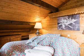 Une chambre à coucher dans une cabane en bois, avec un lit, une table de chevet dotée d’une lampe et un tableau encadré accroché au mur.