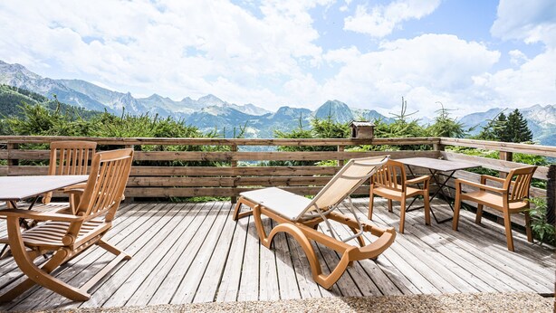 A wooden deck with outdoor furniture, a table, and chairs, overlooking a mountainous landscape. - Chalet Farapreu – Alpine Escape and Absolute Comfort in Manigod (Manigod)