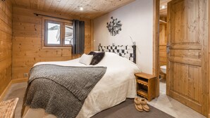 Une chambre à coucher aux murs lambrissés, comprenant un lit, une petite table de chevet, un luminaire fixé au mur et une porte.