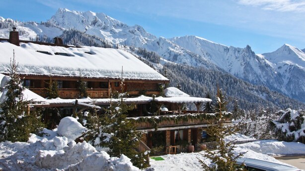 A wooden chalet with a snow-covered roof, surrounded by snow-laden trees and mountains. - Chalet 'Pesse' with Mountain View, Private Jacuzzi & Shared Pool (Summer Only) (Manigod)