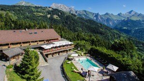 A mountain lodge with a pool, outdoor seating, and a view of the surrounding mountains. - Chalet 'Pesse' with Mountain View, Private Jacuzzi & Shared Pool (Summer Only) (Manigod)