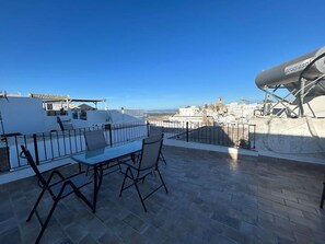 A rooftop terrace with a table and chairs, a satellite dish, and a view of a coastal town. - Apartment 'Casa Andres' with Mountain View, Private Terrace and Wi-Fi (Vejer de la Frontera)