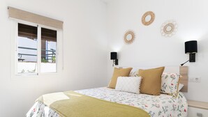 A bedroom with a bed, a window, wall-mounted lamps, and decorative wall art.