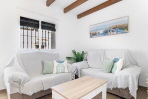 A living room with a white sofa, a wooden coffee table, a window with metal bars, a plant, and a painting on the wall. - Apartment 'Casa Andres' with Mountain View, Private Terrace and Wi-Fi (Vejer de la Frontera)