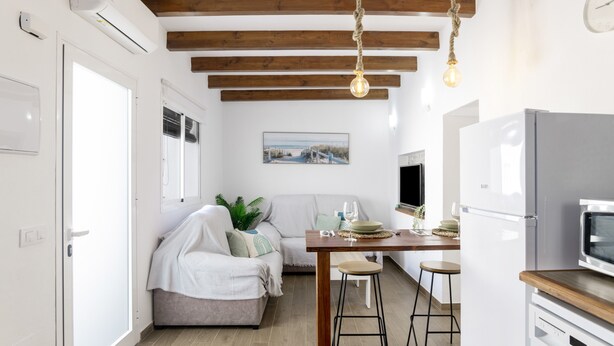 A modern kitchen with a white refrigerator, wooden ceiling beams, and a dining area with a table and chairs.