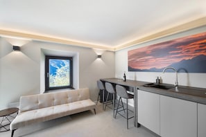 A modern kitchen with a bar area, a sofa, and a large window.