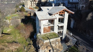 A stone building with a sloped roof, a wooden balcony, and a small garden area.