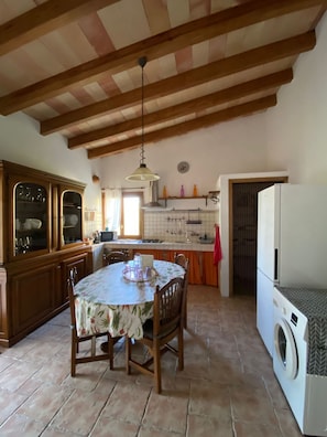 Une cuisine avec des poutres en bois, une table à manger avec des chaises, un lave-linge et un espace pour l’évier.