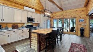 A spacious kitchen with wooden cabinets, a central island, and a dining area with chairs. - Sunset Serenity (Waterfront on Moosehead Lake!) (Greenville)