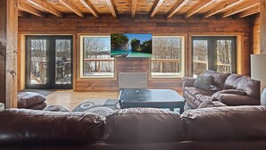 A cozy living room with a wooden ceiling, large windows, and a leather sofa. - Lake View Lodge (Waterfront in Town!) (Greenville)