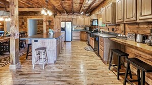 A rustic kitchen with wooden cabinets, a central island, bar stools, and a refrigerator. - Lake View Lodge (Waterfront in Town!) (Greenville)