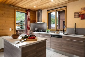 A modern kitchen with wooden cabinetry, a central island, and a view of the outdoors. - Chalet 'Snow Mountain' with Mountain View, Balcony and Wi-Fi (Les Belleville)