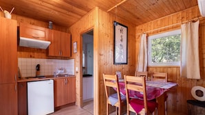 Interior de una cabaña de madera con cocina, comedor y ventana con cortinas.