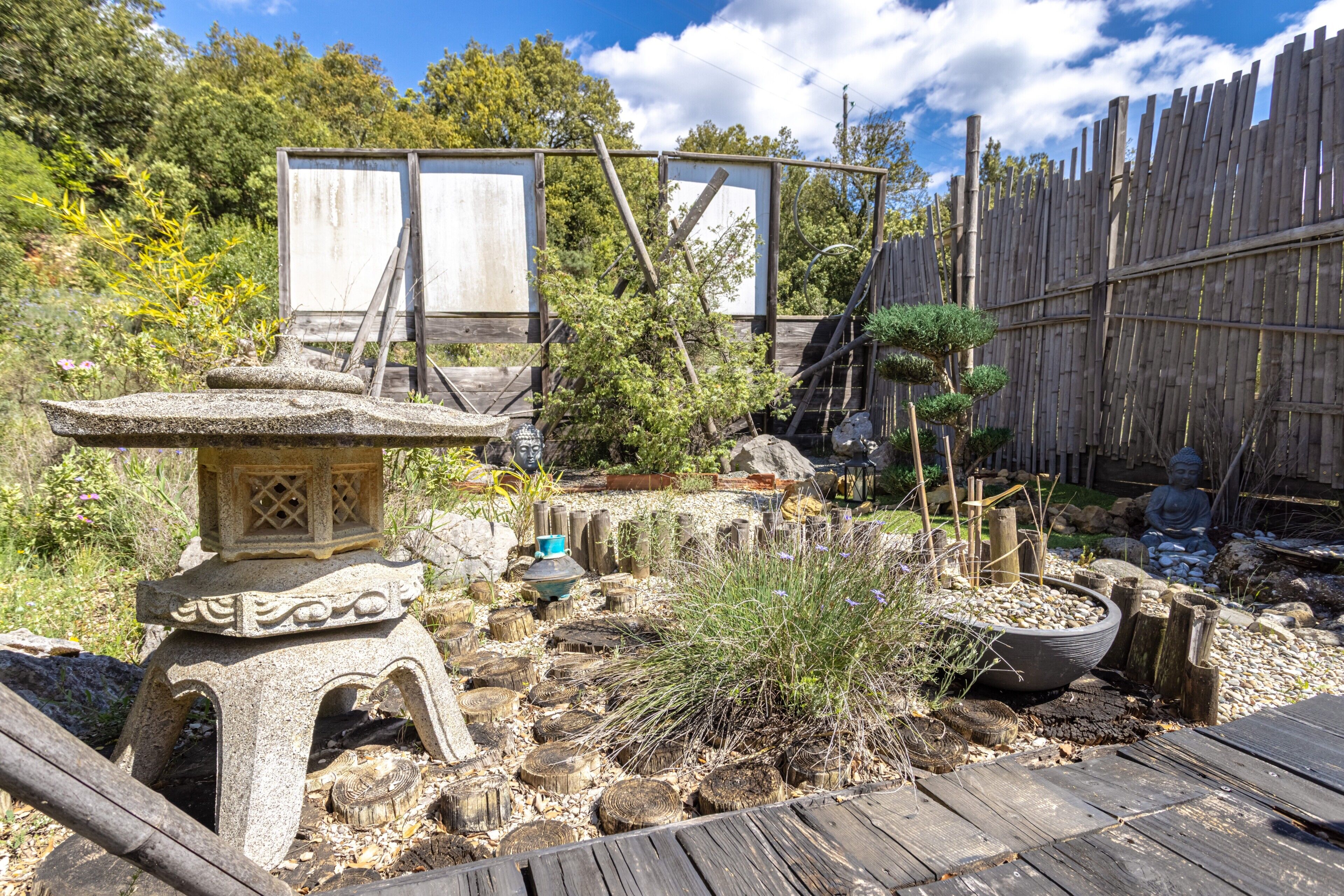 Un jardin agrémenté d’une lanterne en pierre, d’une clôture en bois et de diverses plantes.
