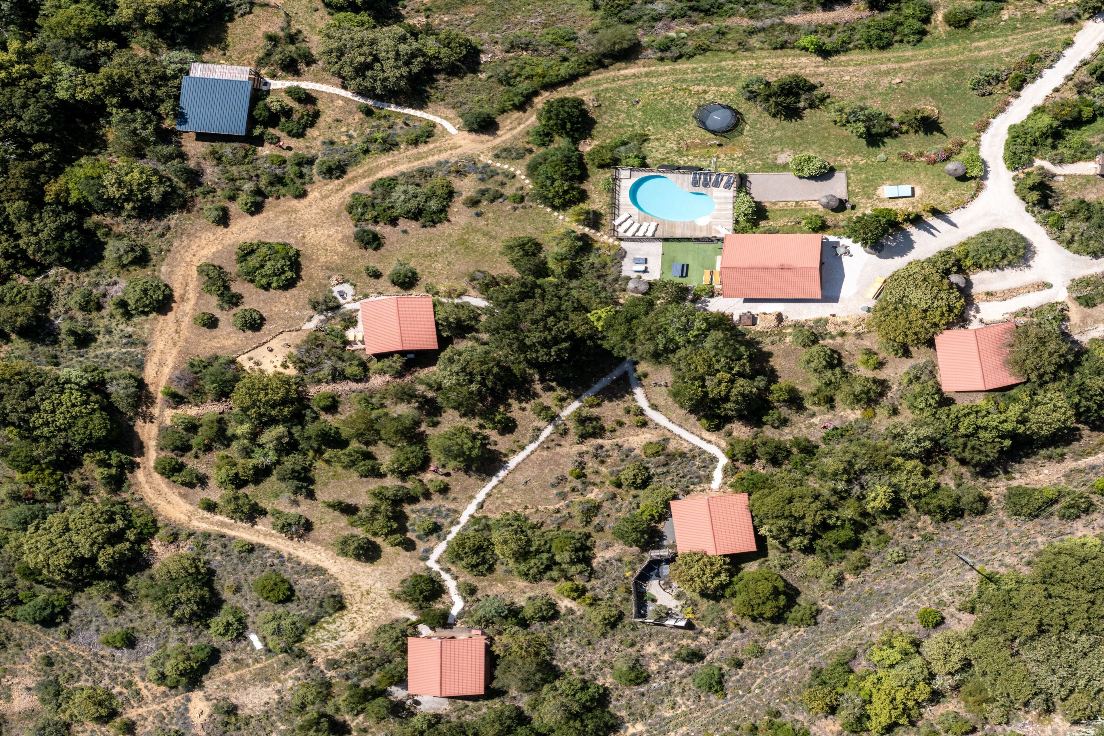 An aerial view of a property with multiple buildings, a swimming pool, and a winding path.