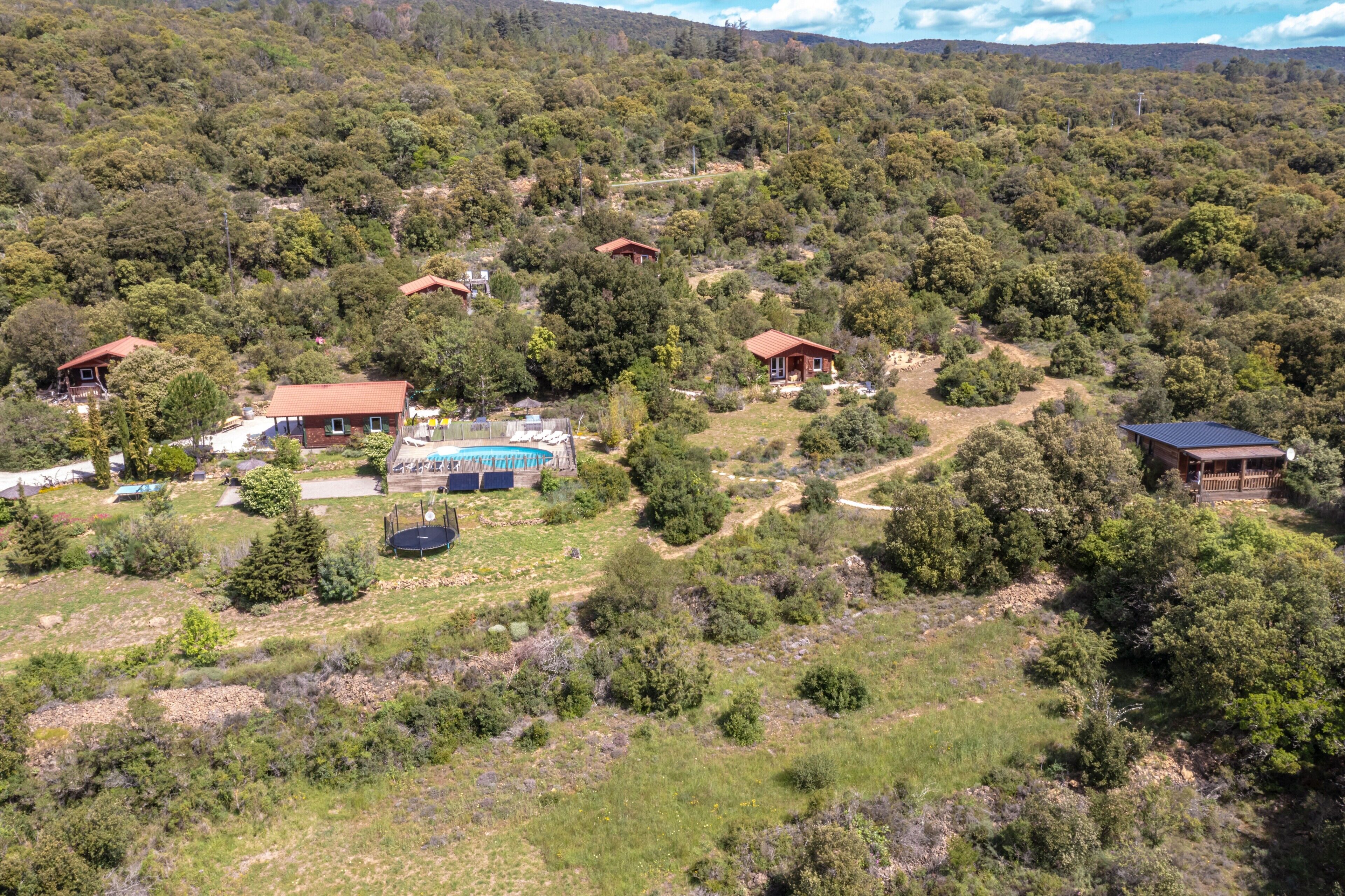A hillside property with multiple cabins, a swimming pool, and a clear view of the surrounding forest.