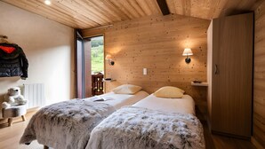 Ein Zimmer mit Holzwandverkleidung, zwei Betten, einem Teddybären, einem Kleiderständer und einer Lampe.