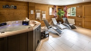 Ein Spa-Raum mit Whirlpool, zwei Massagesesseln, Holzwänden und einem Fenster mit Blick auf Bäume.