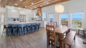 A modern kitchen with a wooden ceiling, white cabinets, and a large island with bar stools. - NEW HOME! AMISTAD IS AN UPSCALE 6BD/4BA HOME W/GULF & CANAL VIEWS, PRIVATE POOL! (Mexico Beach)