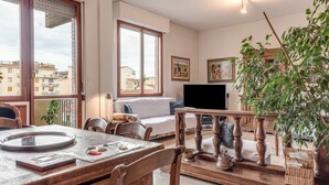 Una sala de estar con sofá, televisión, mesa de comedor con sillas, una mesa de centro de madera y balcón con planta.