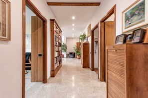 A hallway with wooden doors, a bookshelf, a potted plant, and a desk with a chair.