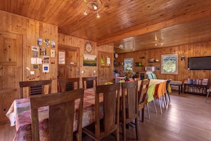 Interior em madeira com sala de jantar, cozinha e televisão.