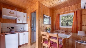 A wooden cabin interior with a kitchen, dining area, and a window with curtains.