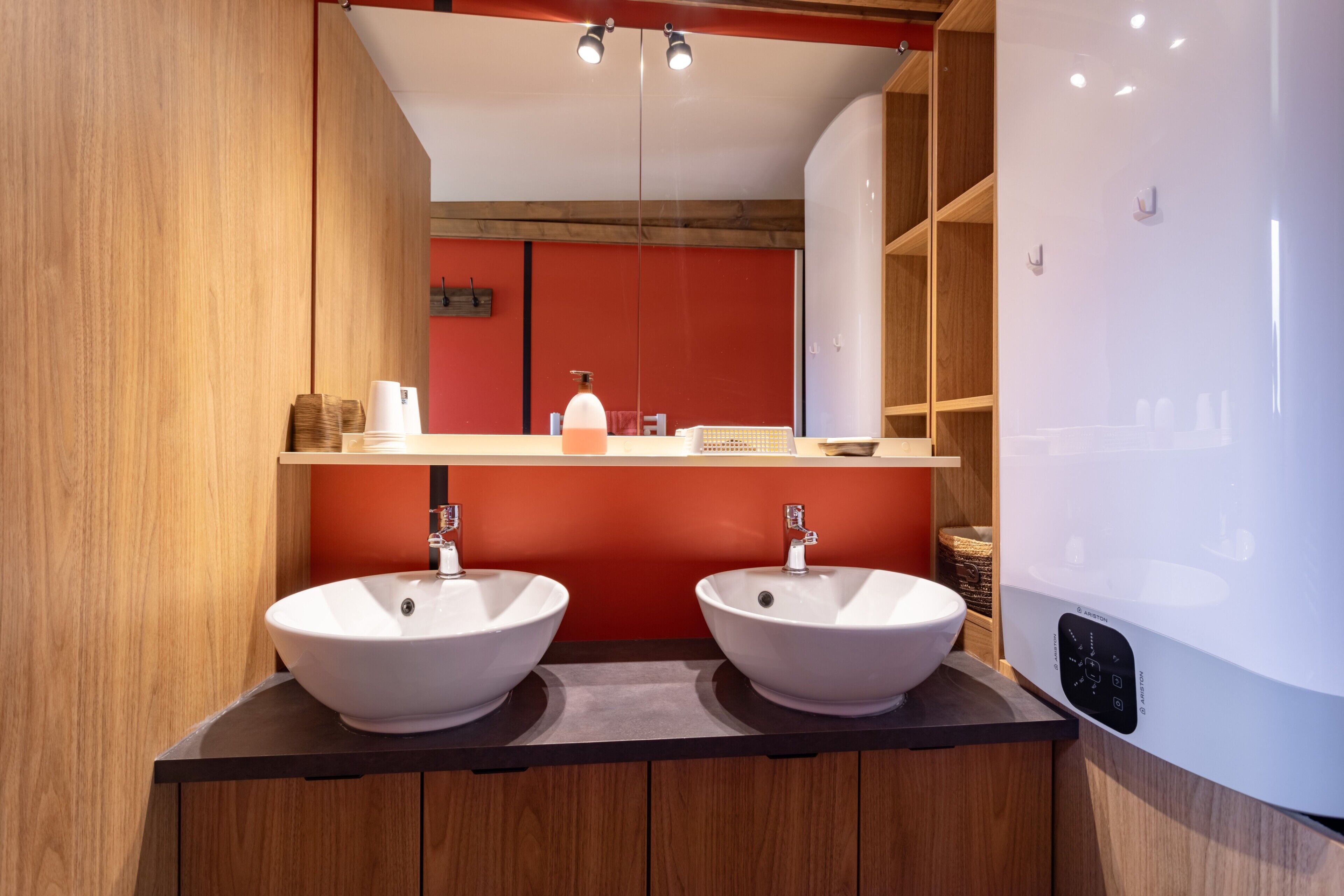 Un bagno moderno con due lavabi bianchi, uno specchio e una parete di accento rossa.