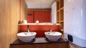 Un bagno moderno con due lavabi bianchi, uno specchio e una parete di accento rossa.