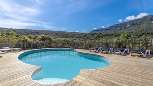 A wooden deck with a swimming pool, lounge chairs, and a mountainous backdrop. - Chalet 'Canada' with Mountain Views, Shared Pool and Private Garden (Rouffiac-des-Corbières)