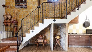 Una escalera con barandilla negra, una zona de cocina con estufa y una mesa de comedor con cerámica.