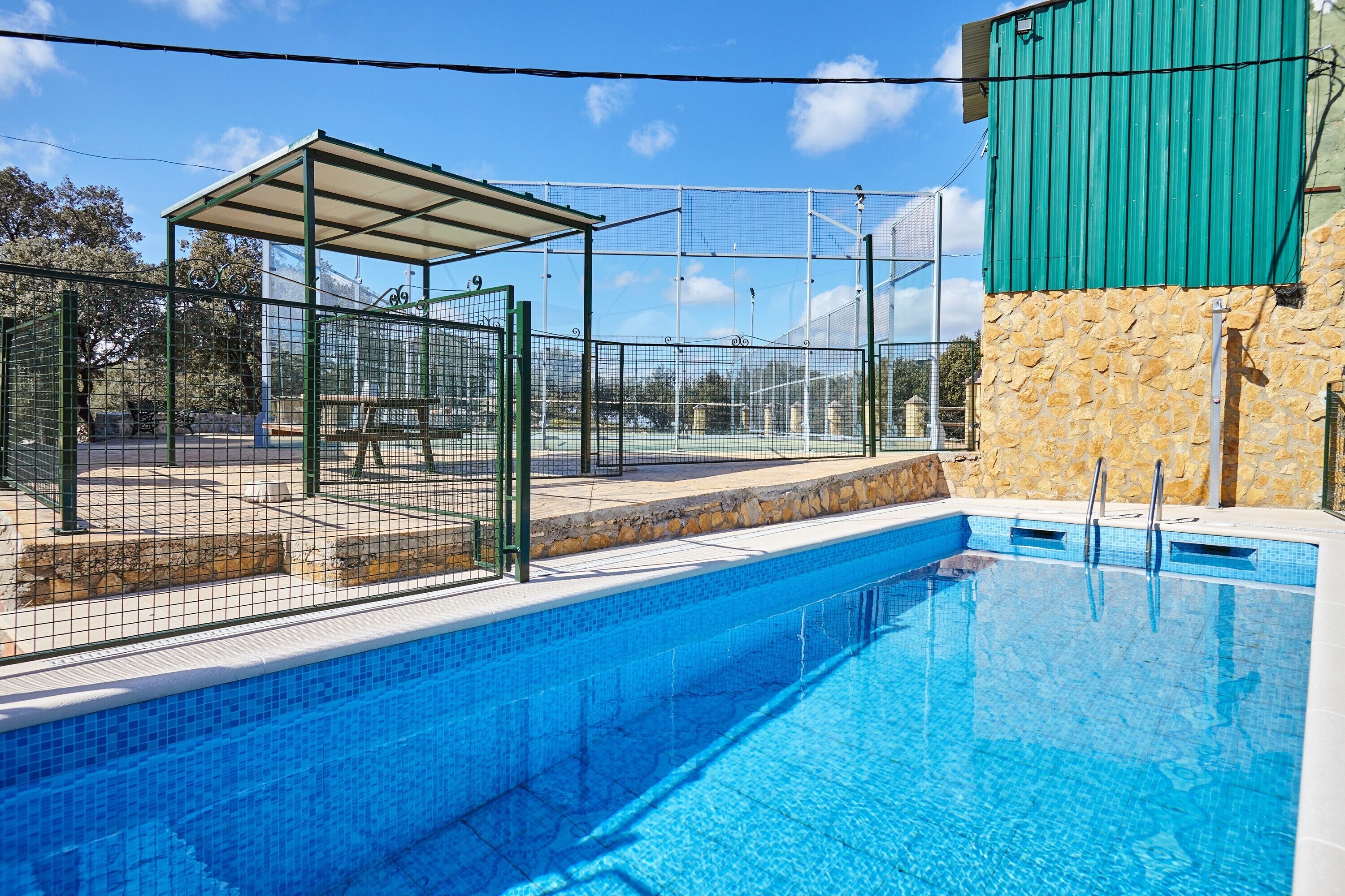 A swimming pool with a covered seating area and a stone wall.
