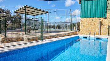 A swimming pool with a covered seating area and a stone wall.