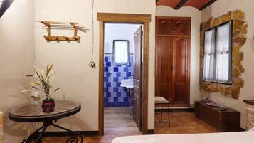 Una habitación con cama, una mesa con un florero, un armario de madera y una pared de piedra.