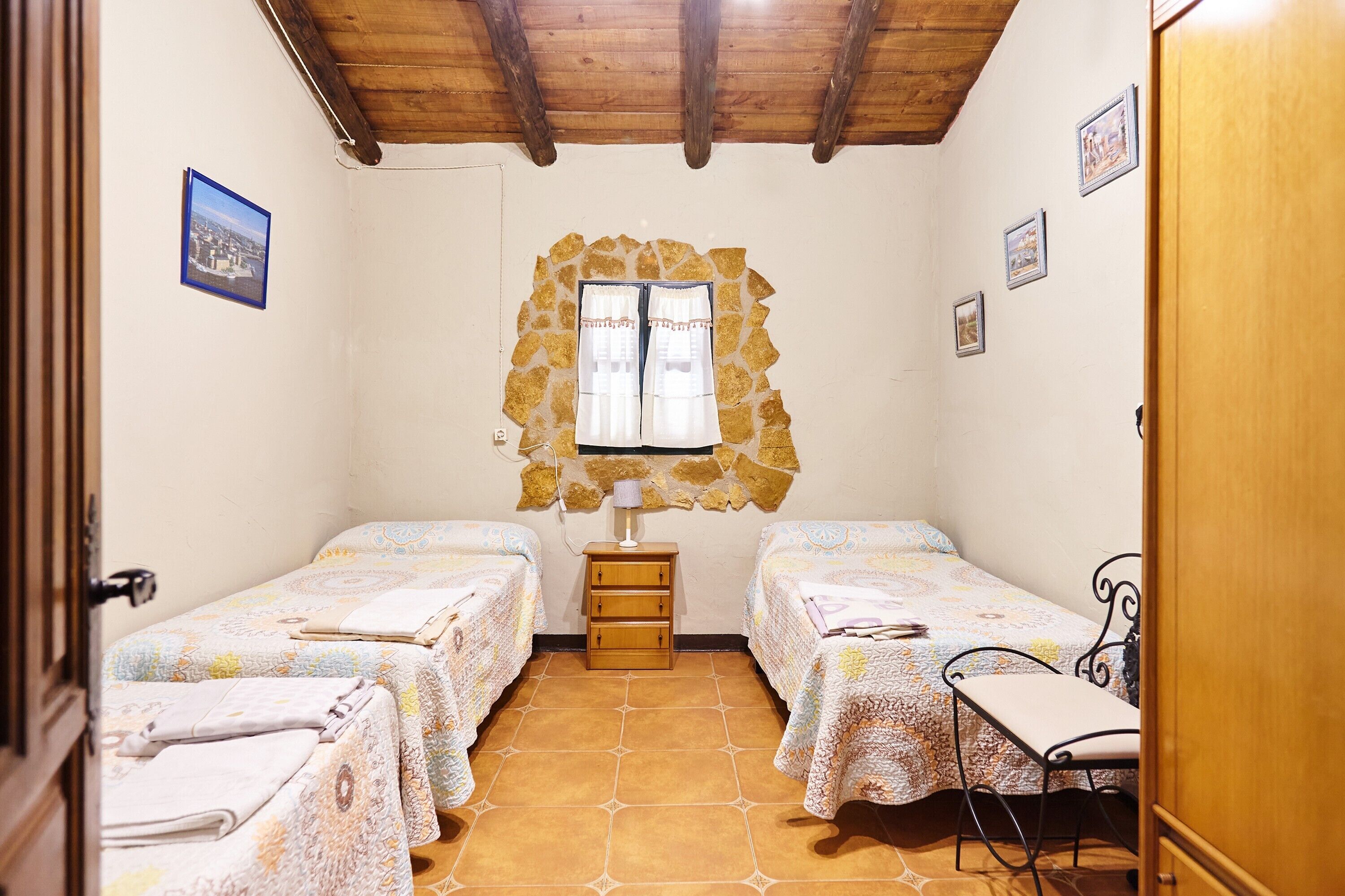 Una stanza con due letti, una finestra con cornice in pietra, un comodino in legno e un tavolino con una sedia.