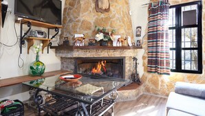 Una chimenea de piedra con un televisor encima, una mesa de vidrio con un mantel individual y una ventana con cortinas.