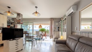 Un salon moderne comprenant un canapé, un téléviseur, un coin cuisine, une table à manger et un balcon avec vue.