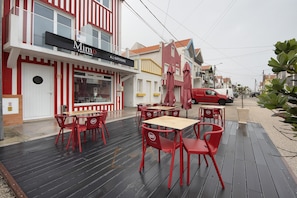 Restaurante com mesas ao ar livre, placa indicando 'Mimo Il gusto italiano' e um carro vermelho estacionado nas proximidades.