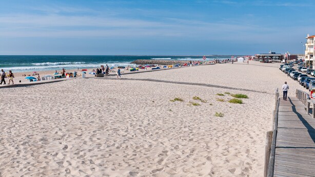 A beach with a wooden boardwalk, umbrellas, and beachgoers.