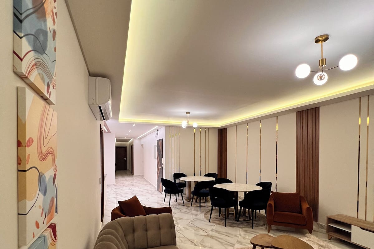 Uma sala de estar moderna com um sofá seccional, uma mesa de jantar com cadeiras e uma pequena mesa de centro.