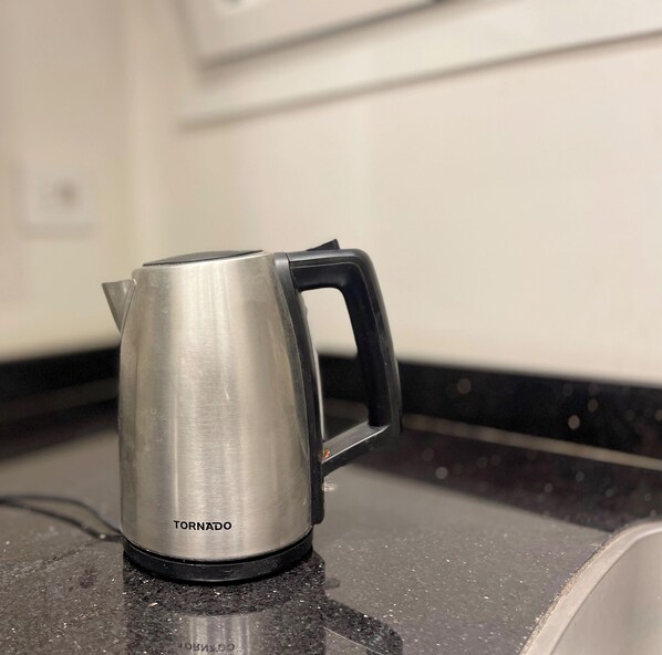 A stainless steel kettle with a black handle on a kitchen counter. - White Palace Serviced Apartments (New Cairo)