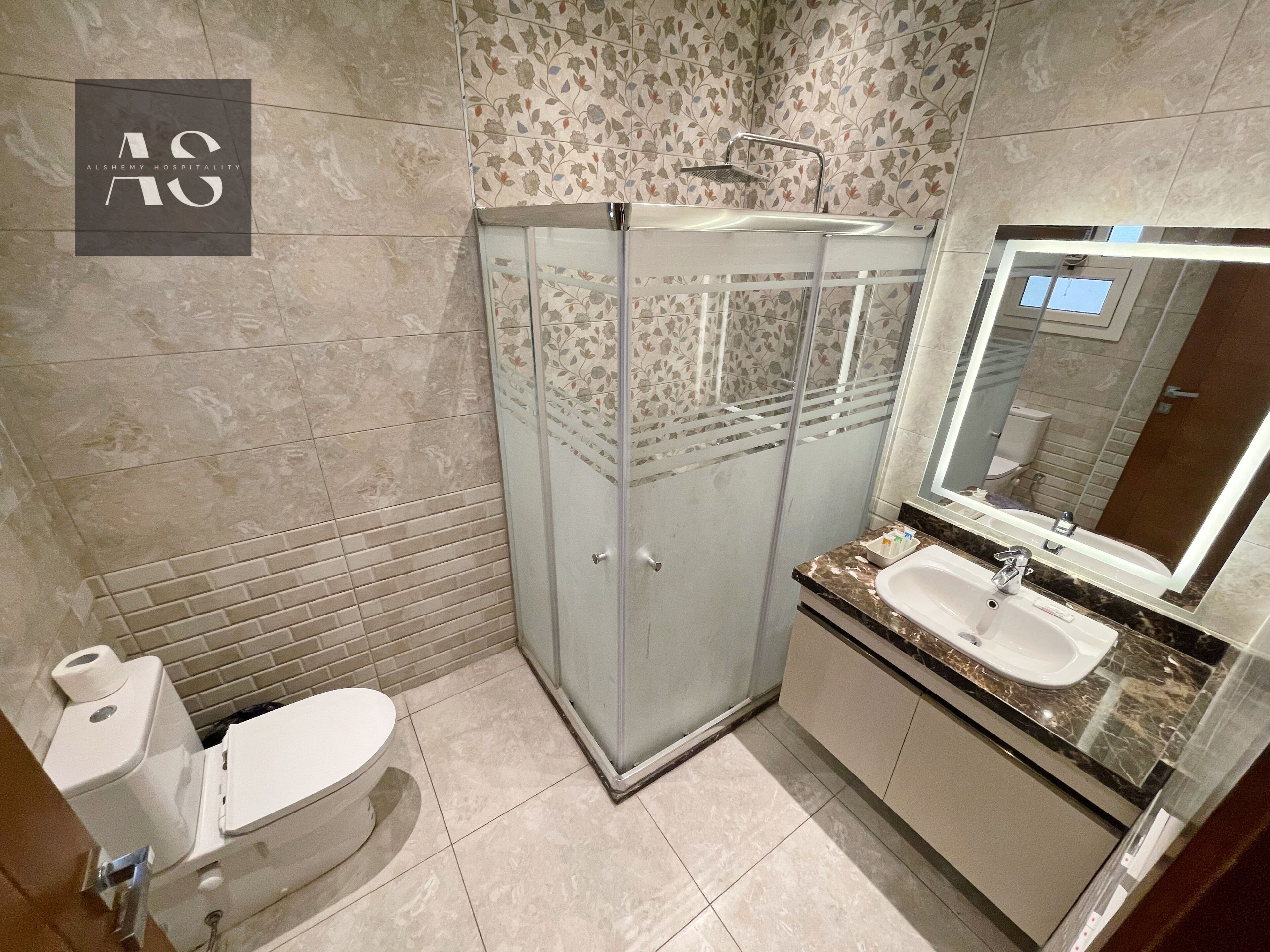 Un baño con inodoro, ducha separada por vidrio, lavamanos y espejo.