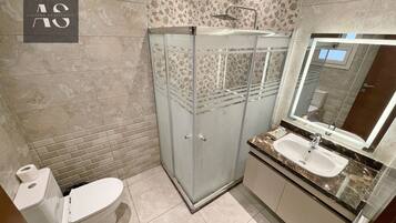 Un baño con inodoro, ducha separada por vidrio, lavamanos y espejo.