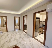 A spacious room with a marble floor, a modern kitchen with a refrigerator and microwave, and a bathroom with a shower and toilet.