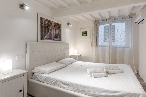 A neatly arranged bedroom with a bed, bedside tables, a wall-mounted picture, and a window with curtains.
