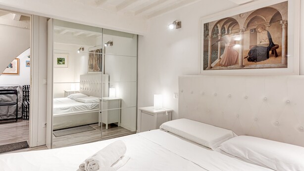 A hotel room with a bed, a mirror, a painting, and a sliding door leading to another room. - Apartment 'Un Bacio A Firenze' with Wi-Fi and Air Conditioning (Firenze)