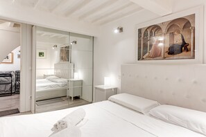 A hotel room with a bed, a mirror, a painting, and a sliding door leading to another room.