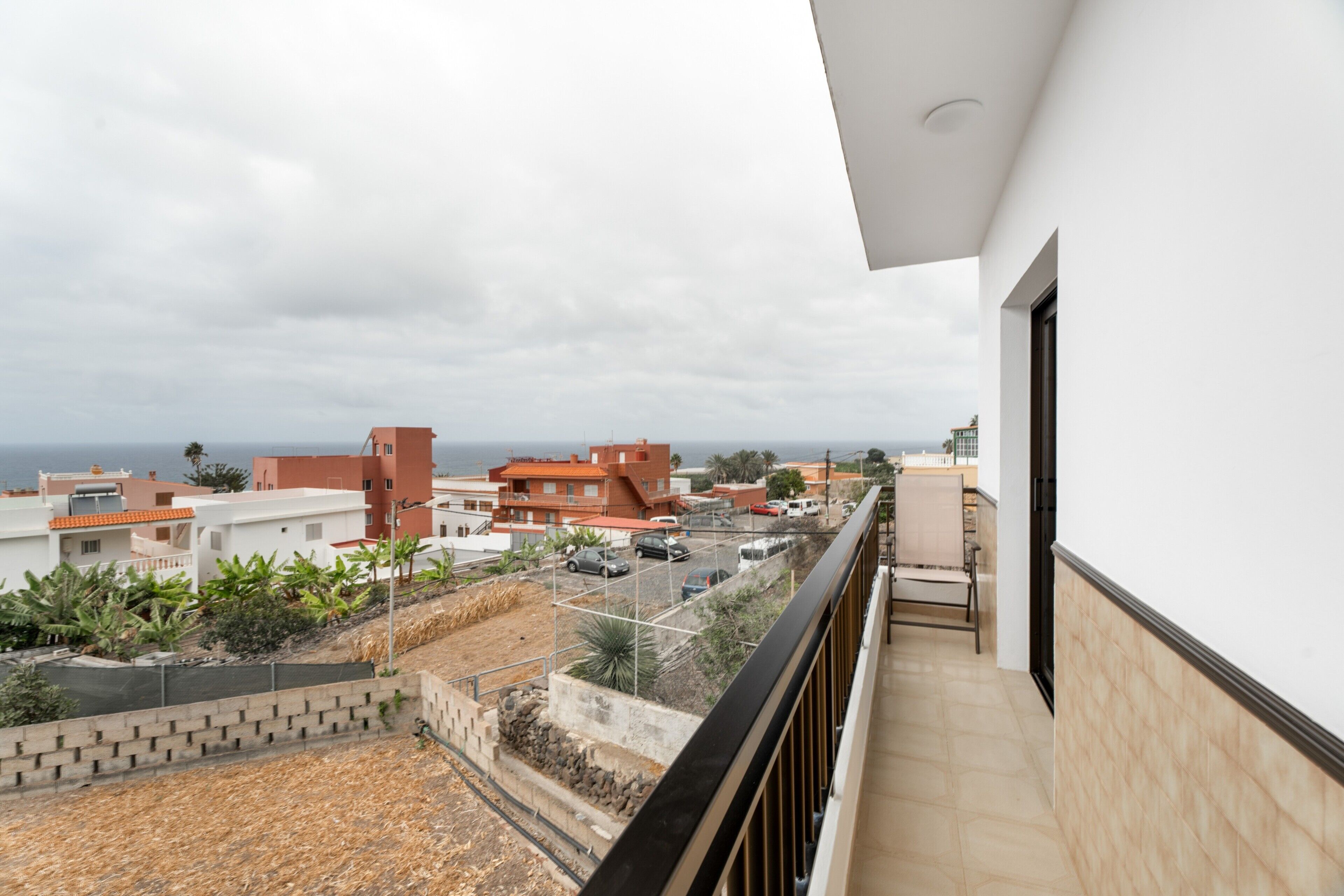 A balcony with a view of a residential area, a paved terrace, and a distant body of water.